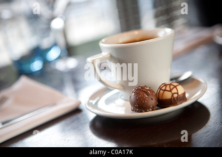 Kaffeetasse mit 2 Pralinen auf der Untertasse auf einem Tisch nach Abendessen Stockfoto