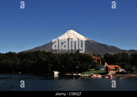 Blauer Himmelsblick von Todos Los Santos See, Volcan Osorno Eis Kegel erhebt sich über Wald, Petrohue Hotel und Fähre Pier, Chile Stockfoto