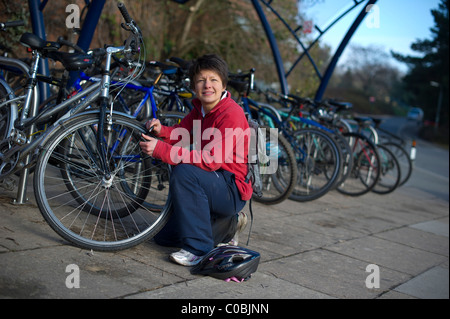 Eine junge weibliche Grad Student sperren Sie ihr Fahrrad in einem Bikepark auf dem Campus an der University of Exeter, Devon. Stockfoto