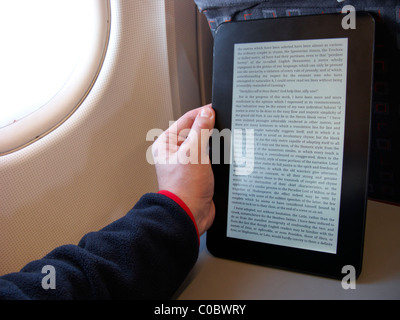 Mann liest einen elektronisches Ebook-Reader an Bord eines Flugzeugs Stockfoto