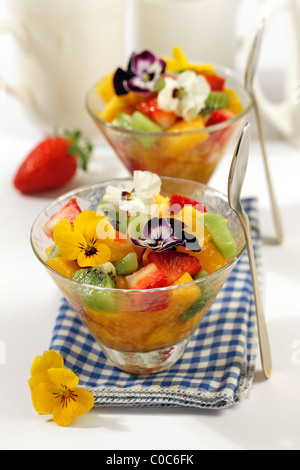 Obstsalat mit essbaren Blüten. Rezept zur Verfügung. Stockfoto