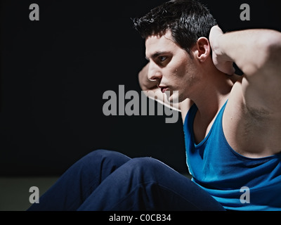 junge Kaukasischen Männchen blau Sportswear trainieren Bauchmuskeln auf schwarzem Hintergrund, wegschauen. Stockfoto