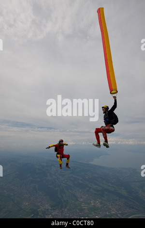 Fallschirmspringer hält eine orange Luftschlauch über schönes Land Scape Landschaft. Die anderen Taucher Mädchen ist herumfliegen in Sit Lage. Stockfoto