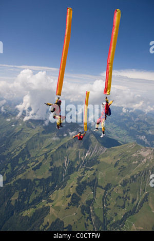 Fallschirmspringer mit Orangen und gelben Luftschlauch fallen durch den Himmel über grüne Berge und Wolken. Stockfoto
