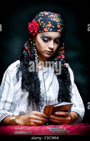 ein Porträt von einer Zigeunerin Wahrsagerin, an einem Tisch sitzen und mit Blick auf die Tarot-Karten, die sie in ihren Händen hält. Stockfoto