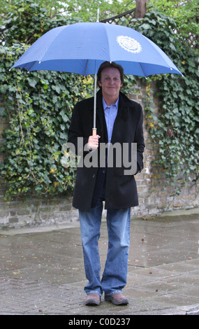 Sir Paul McCartney stellt für Fotografen, als er nach Hause im Regen geht, geschützt von einem großen blauen Schirm London, England- Stockfoto