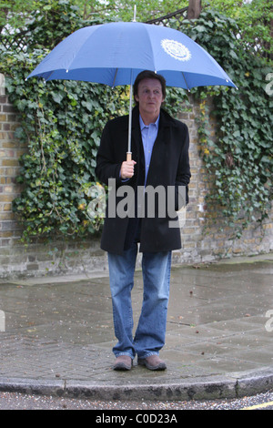 Sir Paul McCartney stellt für Fotografen, als er nach Hause im Regen geht, geschützt von einem großen blauen Schirm London, England- Stockfoto