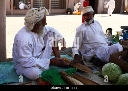 Omanische Männer sitzen im Schatten und verkaufen Obst und Gemüse durch den Souk in Nizwa, Oman. Stockfoto