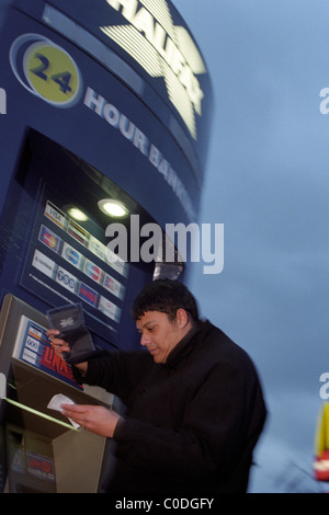 Ein Mann in einen Wintermantel hält seine Brieftasche bei der Überprüfung seiner Kontostand an einem Halifax 24 Stunden Link Cashpoint Automaten Stockfoto