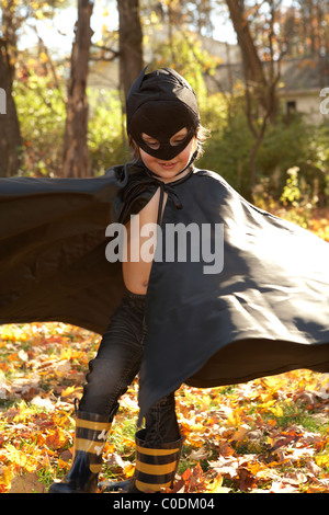 Kid verkleidet wie Batman spielen in den Blättern Stockfoto