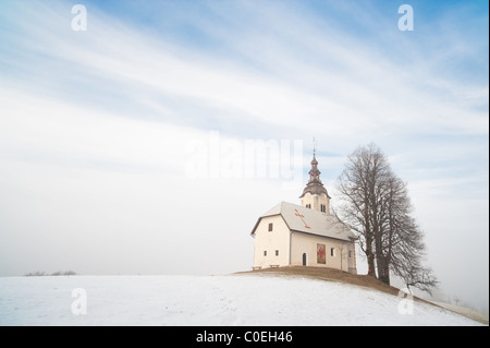 Kleine Kirche auf verschneiten Hügel. Slowenien, Skofja Loka Bereich, St. Andrej Church. Stockfoto