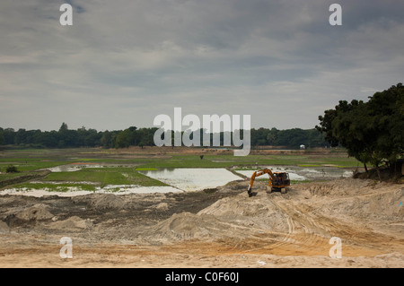 JCB Bagger arbeiten auf einer Baustelle im Vordergrund, mit Reisfeldern in Bangladesch im Hintergrund Stockfoto