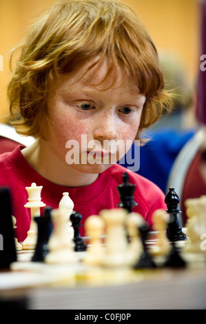 Ein 7 Jahre alter Junge denkt, bevor er seinen nächsten Schritt Schach spielen macht. Stockfoto