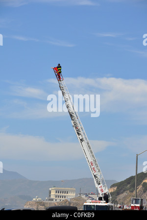 Eine einzelne Feuerwehrauto-Leiter bei voller Streckung mit einer unbekannten Person gegen ein strahlend blauer Himmel Stockfoto