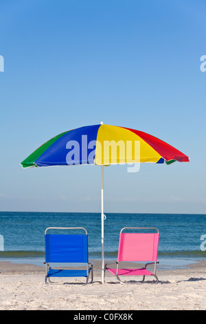 Rosa und blaue Liegestühle am Strand unter einem bunten Regenschirm oder Sonnenschirm Stockfoto