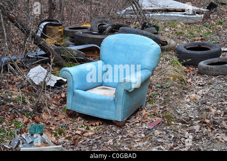 Eine ausrangierte blaue Ledersessel sitzen in den Wäldern umgeben von Reifen, Müll und Schutt. Stockfoto