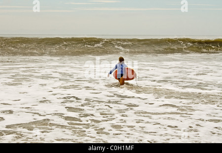 Blonde Frau mit einem Surfbrett nähert sich eine Welle in Jacksonville Beach, Florida Stockfoto