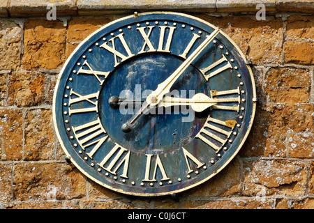 Kunstvoll verzierte Kirchenuhr mit römischen Ziffern auf dem rustikalen, sanften Ironstone-Turm von St. Peter's Church, Knossington, Leicestershire, England, Großbritannien Stockfoto