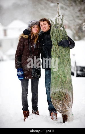 Ein junges Paar mit einem Weihnachtsbaum im Schnee Stockfoto