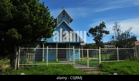 Blauen Schindeln Giebel vorne mit am Straßenrand Weg und Grenze Zaun, der kleinen hölzernen Glockenturm Turm Kirche, Quetalmahue, Chiloé, Chile Stockfoto