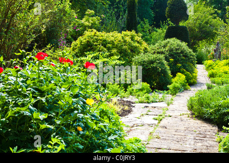 Einen gepflasterten Gartenweg zwischen Sträuchern und Blumen Grenzen in einem englischen Landhaus-Garten im Sommer Stockfoto