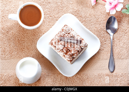 Portion Tiramisu Dessert serviert auf einem weißen geformten Teller und eine Tasse Kaffee mit Sahne Stockfoto