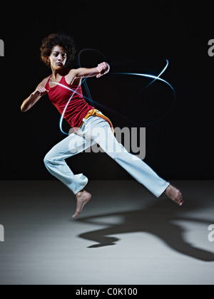 junge Erwachsenfrau lateinamerikanischen tun Capoeira fliegen Kick im Fitness-Studio, mit Streifen von led-leuchten rundum. Stockfoto