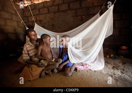 Eine alleinerziehende Mutter sitzt mit ihren Kindern außerhalb der Familie Bett, drapiert mit einem Moskitonetz. Amuria, Uganda, Ostafrika. Stockfoto