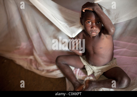 Ein kleines Kind sitzt in einem Bett drapiert mit einem Moskitonetz in Amuria, Uganda, Ostafrika Stockfoto