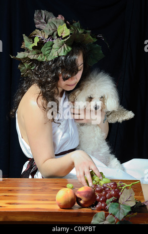 Attraktive Frau gekleidet wie eine weibliche Dionysos, der griechische Gott der Weinlese mit ihrem Bichon Frise. Stockfoto