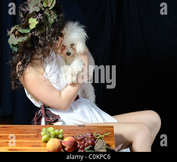 Attraktive Frau gekleidet wie eine weibliche Dionysos, der griechische Gott der Weinlese mit ihrem Bichon Frise. Stockfoto