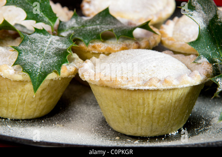 Nahaufnahme von Mince Pies, bestäubt mit Puderzucker auf schwarze Platte mit Holly Zweige Stockfoto