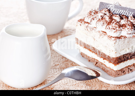 Portion Tiramisu Dessert serviert auf einem weißen geformten Teller und eine Tasse Kaffee mit Sahne Stockfoto