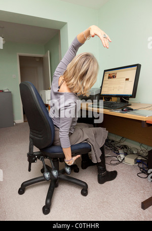 Frau tut Dehnübung vor Büroschreibtisch Stockfoto