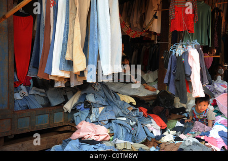 Kind ein Jahr alt, kriechen unter den Haufen von Kleidung auf dem Markt in Sen Monorom, Kambodscha. Stockfoto