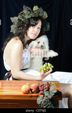 Attraktive Frau gekleidet wie eine weibliche Dionysos, der griechische Gott der Weinlese mit ihrem Bichon Frise. Stockfoto