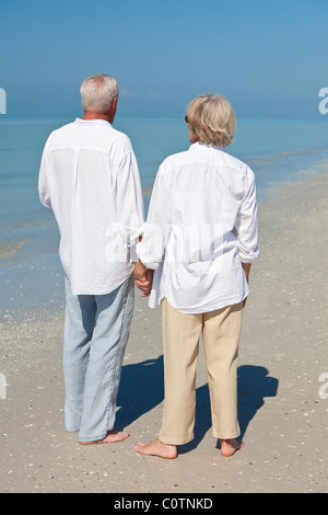 Rückansicht des ein glückliches senior Mann und Frau Paar zusammen Hand in Hand und Blick auf das Meer auf einem einsamen tropischen Strand Stockfoto