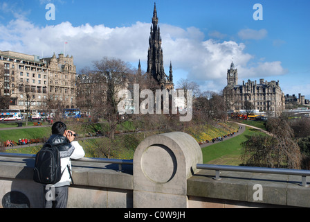 Ein Tourist auf The Mound in Edinburgh Princes Street Gardens, das Scott Monument und Balmoral Hotel zu fotografieren. Stockfoto