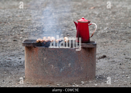 Würstchen und Kaffee auf einen Grill im Freien. Eine altmodische rot Kaffeekanne Vergünstigungen während Würstchen auf dem Grill im freien Kochen Stockfoto