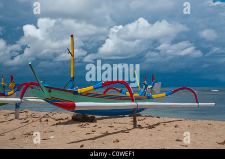 Bunte balinesischen Fischerboot genannt Jukung im Sonnenlicht vor dem Monsun Himmel am Strand von Sanur, Bali-Indonesien Stockfoto