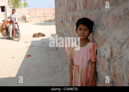 Portrait von Mädchen lehnte sich an der Wand in Rajasthan mit Vater und schlafenden Hund im Hintergrund Stockfoto