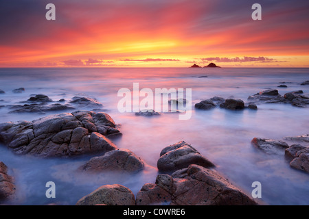 Ein unglaublichen Sonnenuntergang malt den Himmel mit herrlichen Farben als die seidig glatte Meer runden rund um den Felsen am Porth Nanven. Stockfoto