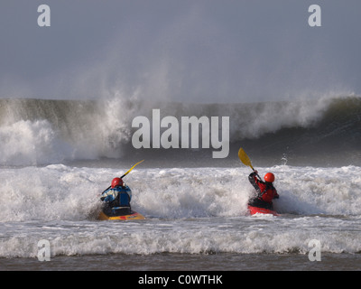 Zwei Surf-Kanuten paddeln vor großen Wellen, Devon, UK Stockfoto