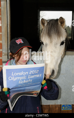 Kleines Mädchen mit einem Londoner Olympic Mütze Blick durch die Spielinformationen über Ticketkauf mit ihrem Haustier pony Stockfoto