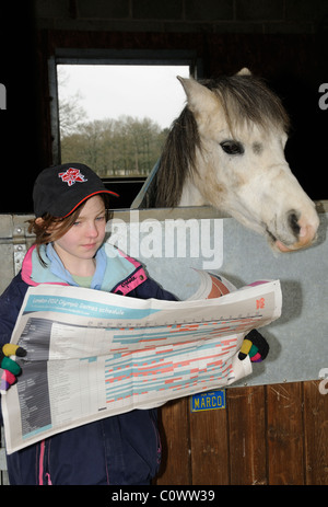 Kleines Mädchen mit einem Olympischen Spiele in London Mütze Blick durch den Spielplan mit ihrem Haustier pony Stockfoto