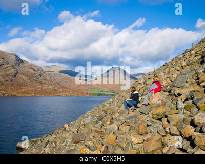 Ein junges Mädchen und junge sitzt auf einem felssturz am Fuße der Geröllhalden mit Blick auf Wastwater in der Nähe von Nether Wasdale im Nationalpark Lake District, Cumbria, England. Stockfoto