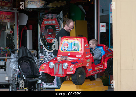 Mann mit einem jungen, Reiten auf einem Childs Fahrt zur Spielhalle Stockfoto