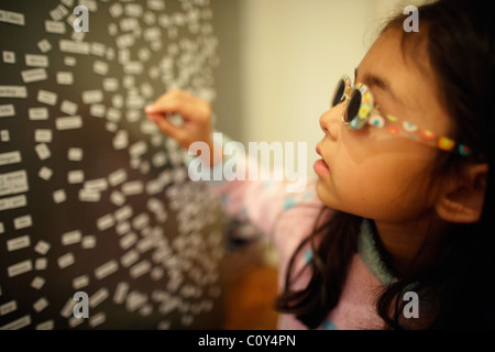 Mädchen trägt Sonnenbrille und spielt mit magnetischen Kühlschrank Wörter Stockfoto