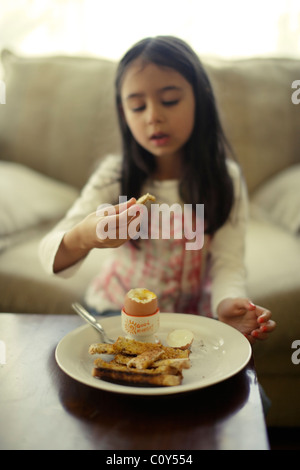 Mädchen isst gekochtes Ei mit Toast Soldaten zum Frühstück Stockfoto