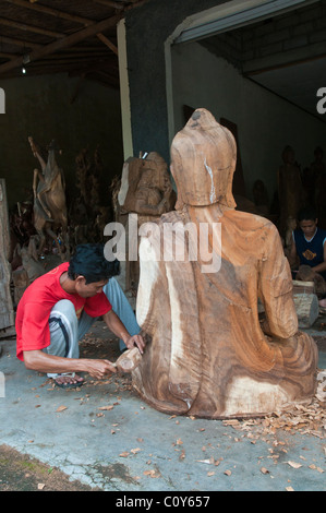 Eine balinesische Handwerker Holzschnitzer bei der Arbeit auf ein schnitzen eines großen sitzenden Buddha in dem Dorf Peliatan Stockfoto